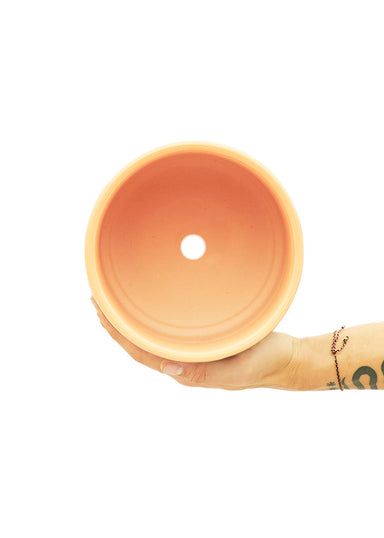 7" Wide Peach Cylindrical Ceramic Planter with a white background with a hand holding it to show the top view